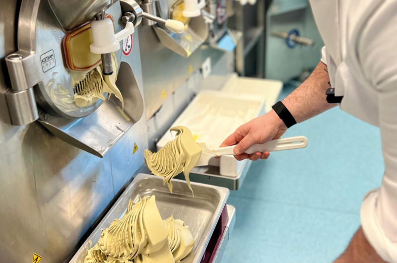 The image shows a member of the Gelato Academy dispensing ice cream into a tray to demonstrate building a base.